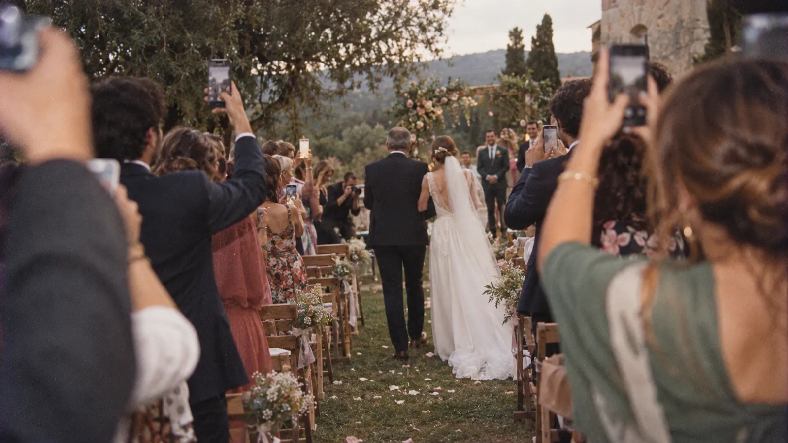Ein Mittelgang bei einer Hochzeit, in dem einige Gäste beim Einzug der Braut ihr Handy hochhalten