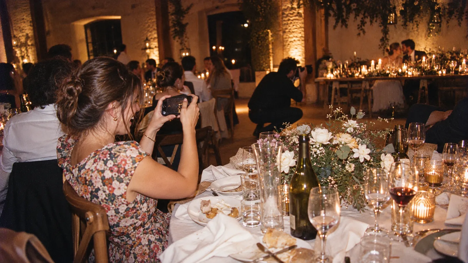 Une invitée photographie la table de mariage au flash pendant que le photographe travaille au fond de la salle