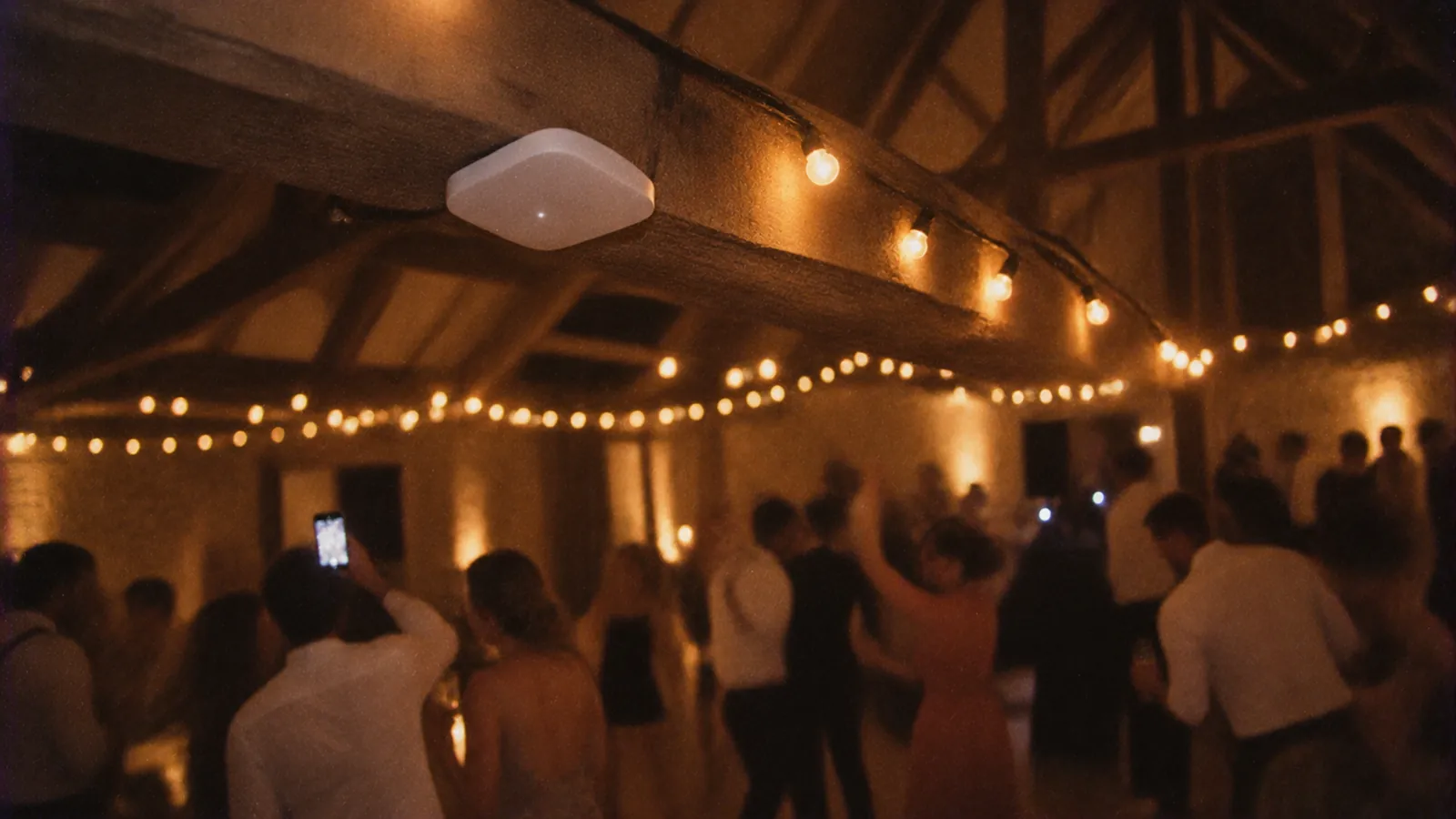 A wifi access point fixed under the beams of a barn set up for a wedding, fairy lights on